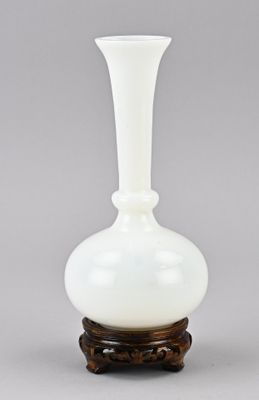 un vase en verre blanc posé sur un socle en bois, sur une surface grise