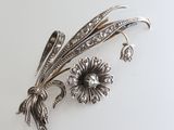 silver plated brooch with flowers and leaves on a white surface