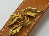 leather belt with a gold flower brooch on a white background
