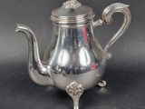a silver tea pot on a stand on a black surface