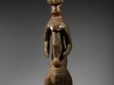une statue en bois représentant un homme debout, les mains sur les hanches