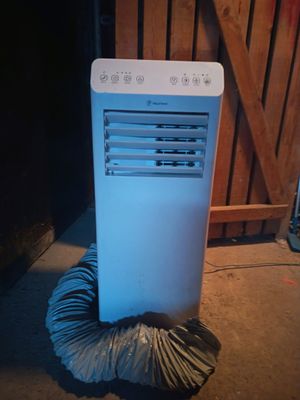 un climatiseur blanc posé par terre à côté d'une clôture en bois