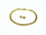 un gros plan d'un bracelet et d'une boucle d'oreille en or posés sur une surface blanche