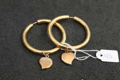 deux boucles d'oreilles en anneau dorées ornées de pendentifs en forme de cœur, sur un fond noir