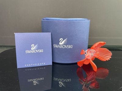 un petit poisson rouge posé sur une table, à côté d'une boîte de Swarovski