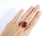 woman ' s hand holding a ring with a pink stone in it