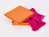 an orange box with a pink scarf in it on a white surface