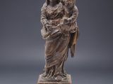 une statue représentant une femme tenant un enfant dans ses bras, posée sur un socle en bois