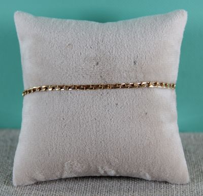 un oreiller blanc sur lequel repose un bracelet à chaîne dorée