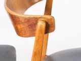 the back of a chair with a wooden seat and arm rests against a white wall
