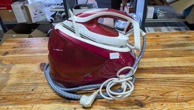 un fer à repasser à vapeur rouge et blanc posé sur une table en bois