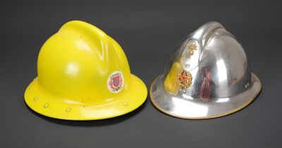 un casque de chantier jaune et un autre argenté posés l'un à côté de l'autre sur une surface noire