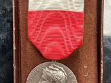une médaille d'argent dans une boîte ornée d'un ruban rouge, blanc et bleu