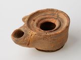 un vase marron troué posé sur une surface blanche
