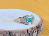une image représentant une bague en or sertie d'une émeraude et de diamants, posée sur un morceau de bois