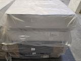 Des cartons contenant des matelas sont empilés les uns sur les autres dans un entrepôt