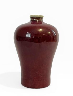 un vase rouge posé sur une surface blanche