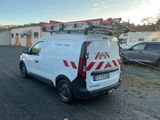 une camionnette blanche garée sur un parking, avec une échelle posée sur le toit