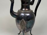 a silver tea pot with a peacock handle on a stand