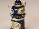 une théière bleue et dorée avec son couvercle, posée sur une table blanche