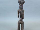 une vieille statue en bois représentant un homme assis sur un tabouret