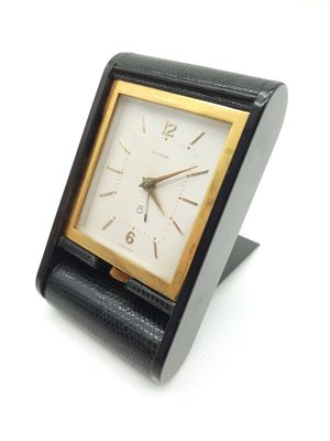 une petite horloge noire avec un cadran doré sur un fond blanc