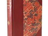 an old book with a red cover sitting on top of a white surface