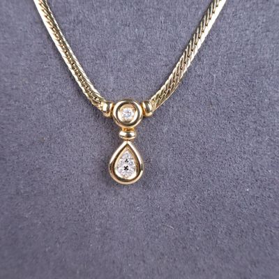 a close up of a gold necklace with a tear shaped diamond