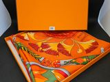 une boîte orange avec une écharpe et un mouchoir assortis, posée sur une chaise noire