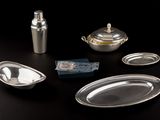 a silver plate with a spoon, a bottle, and other silverware on a table