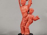 une statue orange représentant une femme tenant un enfant dans ses bras, posée sur un socle noir