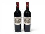 two bottles of red wine sitting next to each other on a white surface