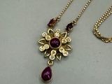 necklace with a purple stone and a gold chain on a white surface