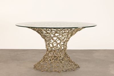 une table en verre avec un piètement en métal doré et un plateau circulaire en verre
