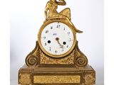 a gold clock with a woman sitting on top of it