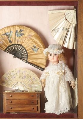 a picture of a doll in a shadow box with a fan