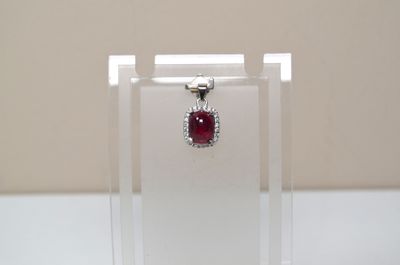 une photo d'un pendentif composé d'une pierre rouge et d'un diamant, présenté dans une vitrine transparente