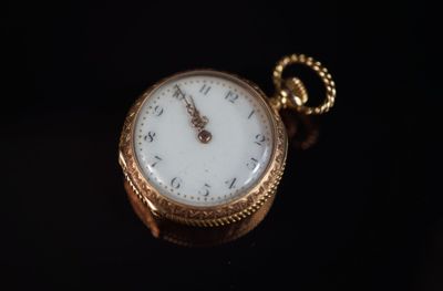 gros plan d'une montre de poche en or sur une surface noire