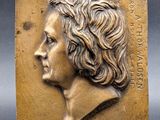 a bronze plaque of a woman ' s head with wavy hair