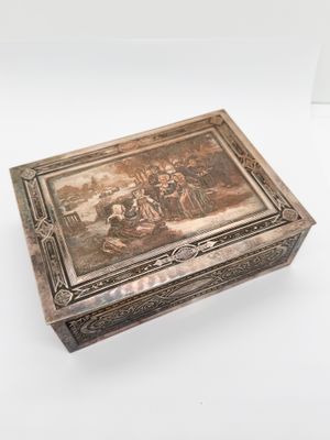 une vieille boîte en argent ornée d'une peinture, posée sur une surface blanche