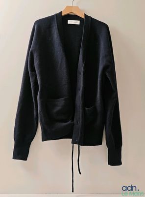 un cardigan noir suspendu à un cintre devant un mur blanc