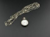 un gros plan d'une montre de poche en argent avec sa chaîne, posée sur une surface noire