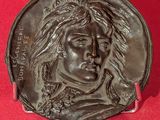 une image représentant un médaillon en bronze orné du visage d'un homme