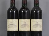 trois bouteilles de vin rouge sont posées sur une table en verre devant un mur gris