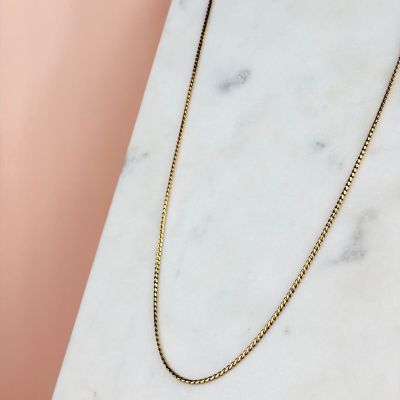 un collier à chaîne en or posé sur une surface en marbre