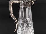 a silver plated glass pitcher with a handle on a table