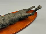statue of a cat laying on a wooden board on a white surface