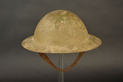 un vieux casque posé sur un support métallique, sur fond gris