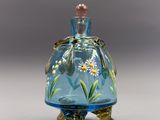 une image représentant un flacon de parfum en verre bleu orné de fleurs