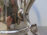 une cafetière en argent posée sur une table, tandis qu'une personne la prend en photo
